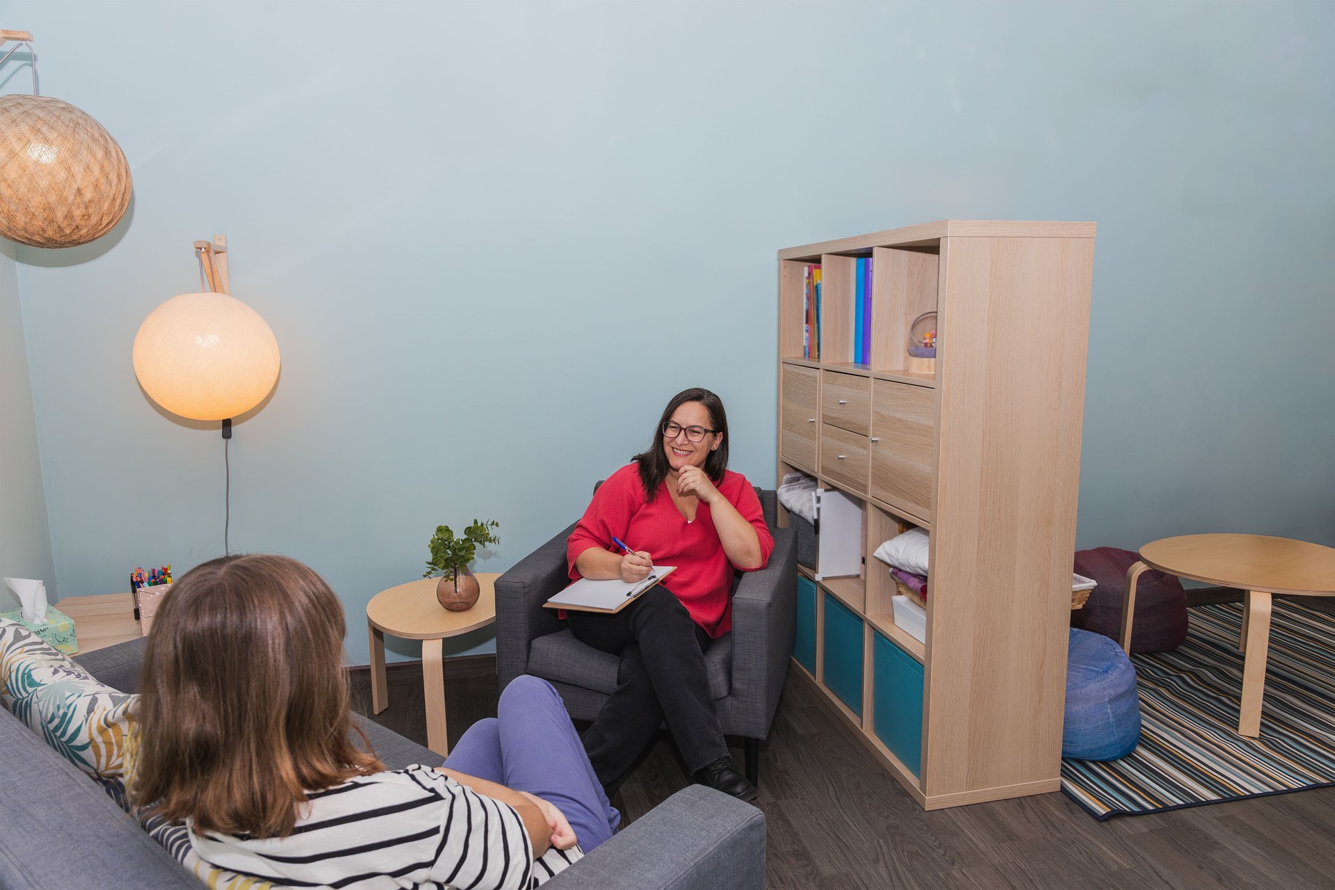 Vista amplia de un consultorio de psicología con una terapeuta tomando notas mientras está sentada frente a un paciente joven. Decoración de estilo escandinavo e iluminación tenue. Espacio de copia. Concepto de espacio terapéutico, confidencialidad y 