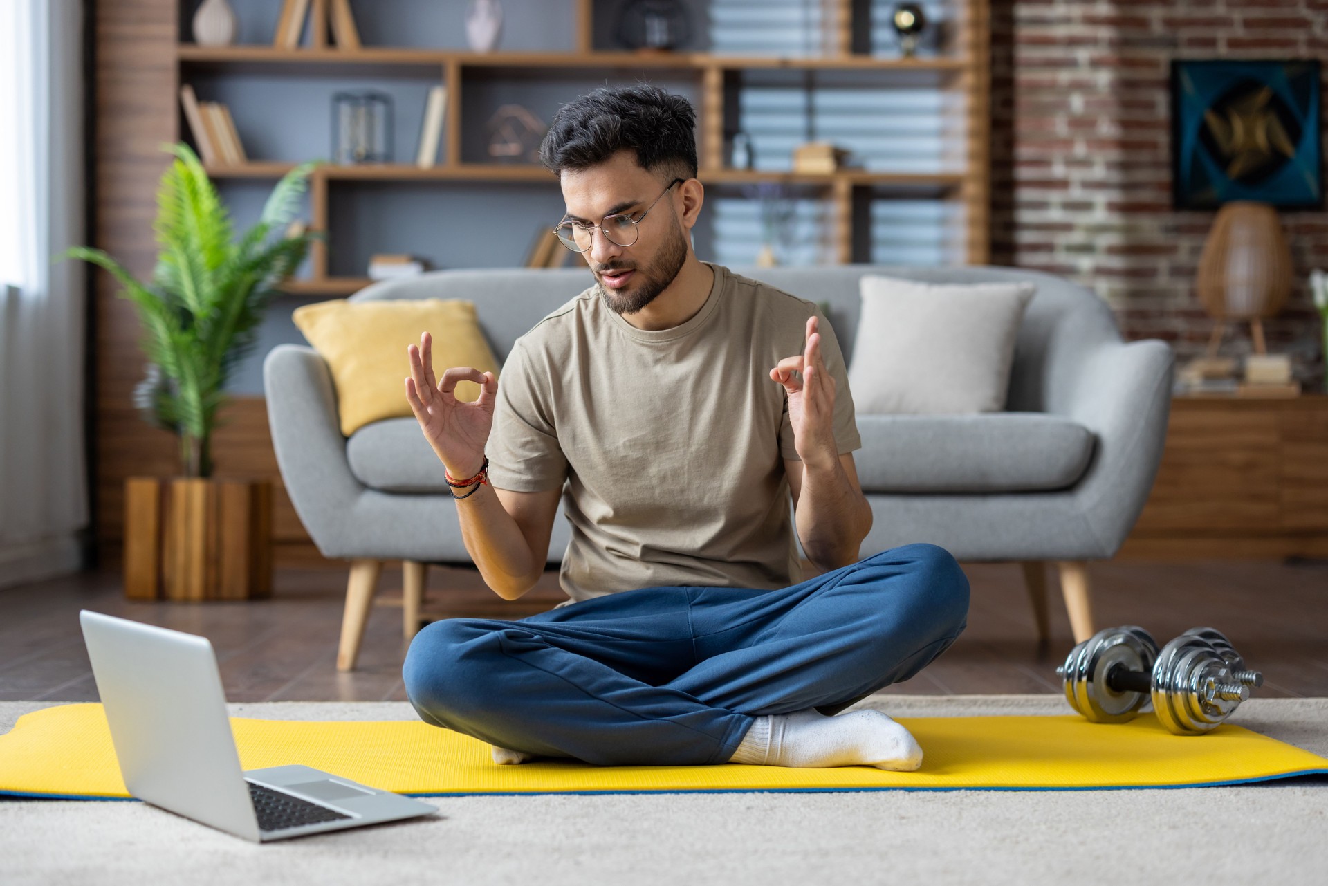 Hombre practicando meditación de yoga en línea usando una computadora portátil en casa para la relajación y la terapia de atención plena