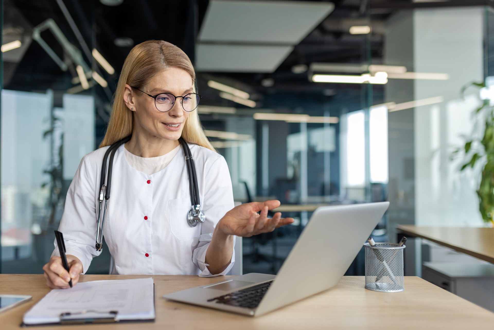 Doctora que realiza una consulta por videollamada utilizando una computadora portátil en un entorno de oficina moderno, fomentando la interacción con el paciente y la innovación en la atención médica a través de la comunicación digital