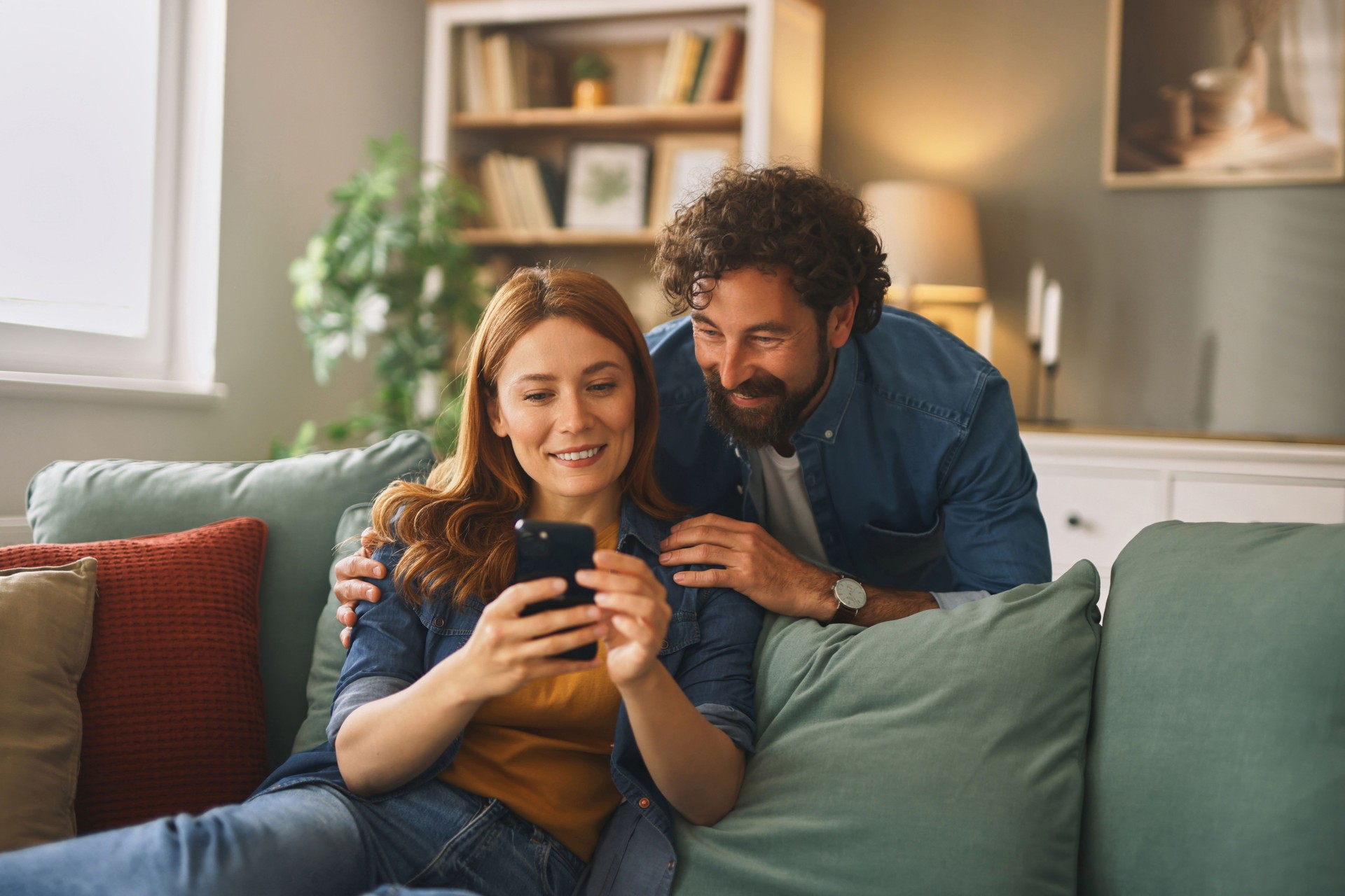 Pareja feliz relajándose en el sofá y navegando por el teléfono inteligente en casa